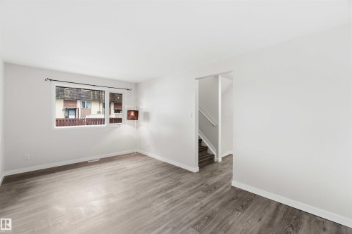 Spacious room featuring wood-finish flooring, white baseboards, and a large window providing natural light - 3312 106 Avenue, Edmonton, AB 