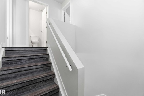 Staircase with dark wood-finish treads and white risers, featuring a white painted handrail and balustrade, with a white toilet visible through an open doorway - 3312 106 Avenue, Edmonton, AB 