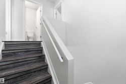 Staircase with dark wood-finish treads and white risers, featuring a white painted handrail and balustrade, with a white toilet visible through an open doorway - 