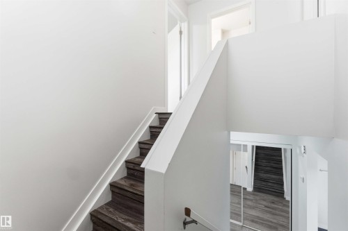 Staircase featuring wood-finish treads and risers, white painted handrails, and bright white walls - 3312 106 Avenue, Edmonton, AB 