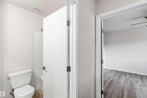 Bathroom featuring a modern toilet, tiled shower surround, and a contemporary white door with horizontal paneling - 3312 106 Avenue, Edmonton, AB 