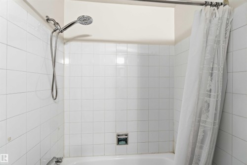 Bathtub shower with white tile surround, chrome fixtures, and a wall-mounted showerhead with handheld sprayer - 3312 106 Avenue, Edmonton, AB 