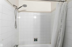 Bathtub shower with white tile surround, chrome fixtures, and a wall-mounted showerhead with handheld sprayer - 