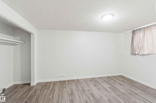 Spacious room featuring wood-finish flooring, white walls, and a recessed closet with shelving - 3312 106 Avenue, Edmonton, AB 