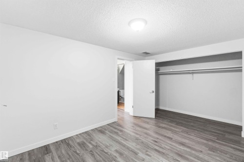 Room featuring wood-finish flooring, white baseboards, a ceiling-mounted light fixture, and an open closet with a hanging rod and shelf - 3312 106 Avenue, Edmonton, AB 