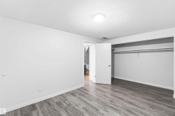Room featuring wood-finish flooring, white baseboards, a ceiling-mounted light fixture, and an open closet with a hanging rod and shelf - 