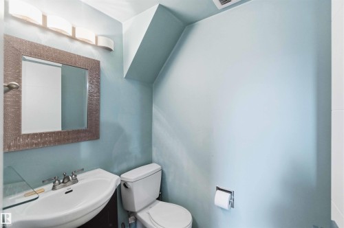 Bathroom featuring a pedestal sink with a chrome faucet, wall-mounted mirror, and overhead vanity lighting - 3312 106 Avenue, Edmonton, AB 