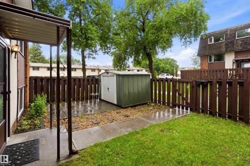 Private outdoor patio featuring a metal storage shed, a manicured lawn, a concrete pathway, and a wooden privacy fence with a gate - 3312 106 Avenue, Edmonton, AB 