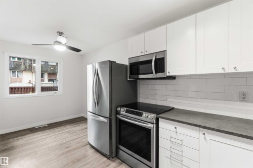 Modern kitchen featuring stainless steel appliances, white cabinetry, a subway tile backsplash, dark countertops, and wood-finish flooring - 3312 106 Avenue, Edmonton, AB 
