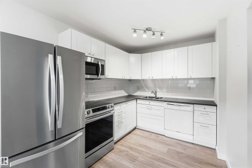 Modern kitchen featuring wood-finish flooring, white cabinetry, dark countertops, and stainless steel appliances including a refrigerator, range, and built-in microwave - 3312 106 Avenue, Edmonton, AB 