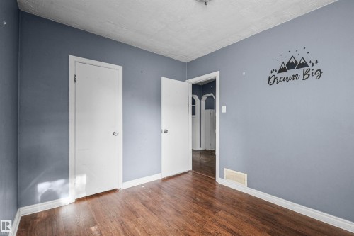 Interior room featuring wood-finish flooring, light blue-gray walls, white trim, and two white doors - 7520 106 Street, Edmonton, AB 