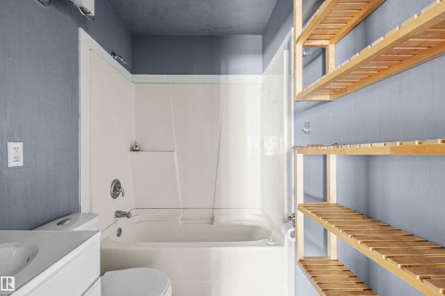 Bathroom featuring a white integrated tub and shower unit, chrome fixtures, a white toilet, and a white vanity with an integrated sink - 7520 106 Street, Edmonton, AB 
