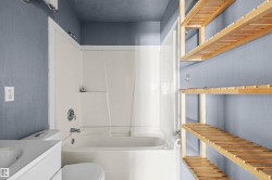 Bathroom featuring a white integrated tub and shower unit, chrome fixtures, a white toilet, and a white vanity with an integrated sink - 