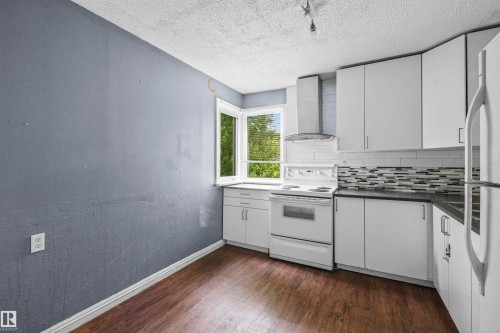 Kitchen featuring white cabinetry, dark countertops, wood-finish flooring, and a decorative tile backsplash - 7520 106 Street, Edmonton, AB 