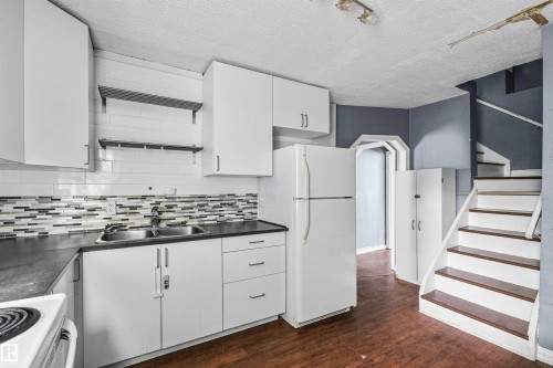 Kitchen featuring white cabinetry, dark countertops, a mosaic tile backsplash, and a double basin sink - 7520 106 Street, Edmonton, AB 