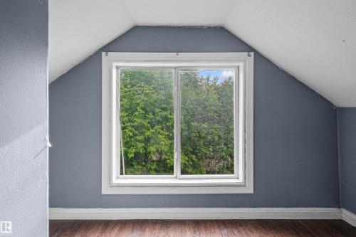Attic space featuring a double-hung window, sloped ceilings, wood-finish flooring, and painted walls - 7520 106 Street, Edmonton, AB 
