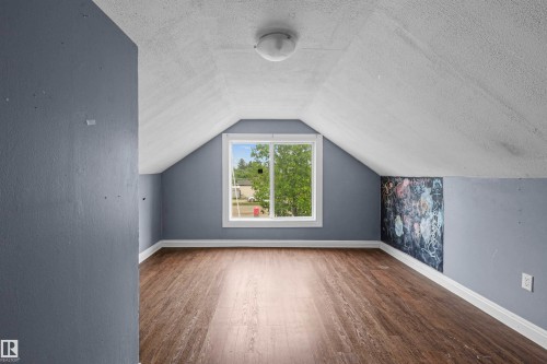 Room featuring wood-finish flooring, a white trim window, sloped ceilings, and a corner accent wall - 7520 106 Street, Edmonton, AB 