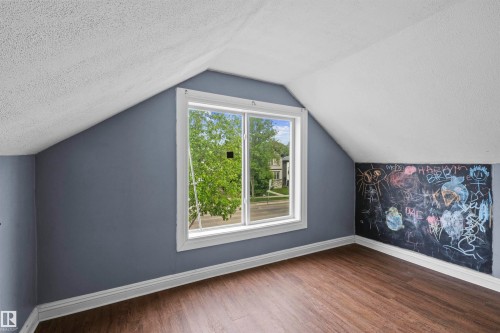 Interior room featuring sloped ceilings, a prominent window with white trim, wood-finish flooring, a chalkboard wall, and painted walls - 7520 106 Street, Edmonton, AB 
