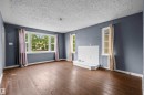 Spacious living area featuring wood-finish flooring, a prominent bay window, and a white built-in fireplace structure - 7520 106 Street, Edmonton, AB 