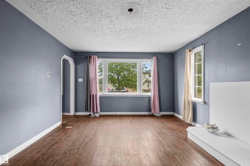 Spacious room featuring wood-finish flooring, a large window with natural light, and an arched doorway - 7520 106 Street, Edmonton, AB 