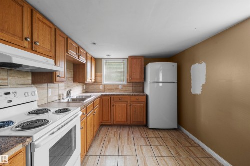 Kitchen featuring wood cabinetry, a double basin stainless steel sink, a tile backsplash, and a window for natural light - 7520 106 Street, Edmonton, AB 