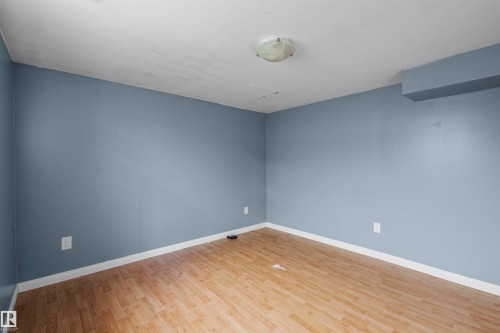 Room featuring light blue walls, wood-finish flooring, white baseboards, and a flush-mount ceiling light fixture - 7520 106 Street, Edmonton, AB 