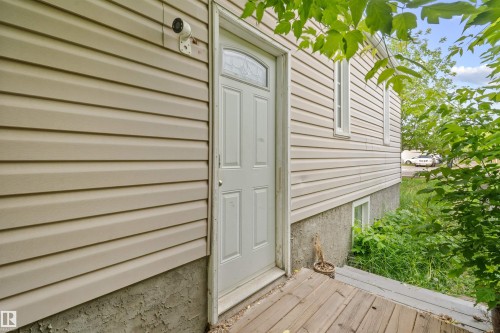 Tan horizontal siding exterior with a white paneled entry door featuring an arched window insert, set on a wooden deck - 7520 106 Street, Edmonton, AB 