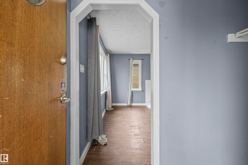 Arched entryway revealing a living area with wood-finish flooring, light blue walls, and multiple windows - 7520 106 Street, Edmonton, AB 