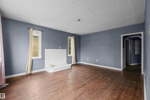 Spacious room featuring wood-finish flooring, light blue walls, and a textured white ceiling - 7520 106 Street, Edmonton, AB 
