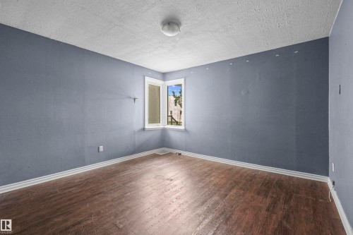 Room featuring wood-finish flooring, white baseboards, and a corner window with white trim - 7520 106 Street, Edmonton, AB 