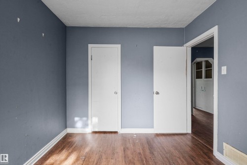 Interior room featuring wood-finish flooring, two white doors, and blue-gray painted walls - 7520 106 Street, Edmonton, AB 