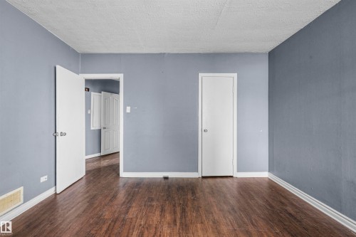 Spacious room featuring wood-finish flooring, light blue wall paint, white trim, and multiple white panel doors - 7520 106 Street, Edmonton, AB 