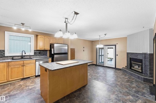 Kitchen and living area featuring a central island, light wood cabinetry, stainless steel appliances, and a tiled fireplace - 17303 107 Street, Edmonton, AB 
