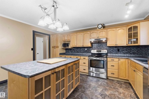 Kitchen featuring light wood cabinetry, stainless steel appliances, a dark tile backsplash, and stone-look flooring - 17303 107 Street, Edmonton, AB 
