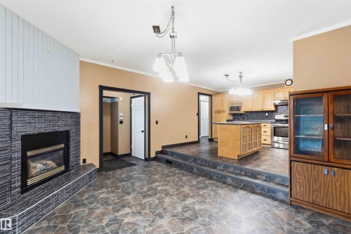 Interior featuring a dark tile fireplace with a white vertical plank accent wall, a two-tier kitchen island, light wood cabinetry, and stainless steel appliances - 17303 107 Street, Edmonton, AB 