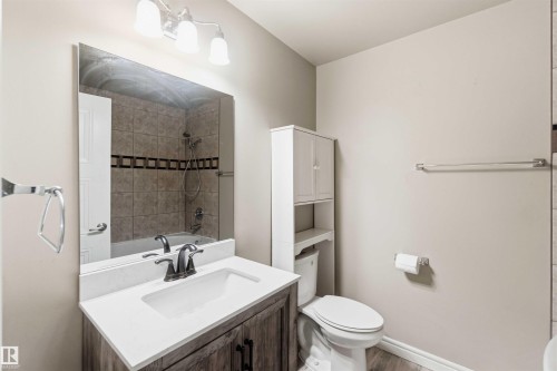 Bathroom featuring a wood-finish vanity with an integrated white sink, a quartz-look countertop, and a chrome faucet - 17303 107 Street, Edmonton, AB 