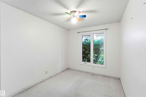 Bright room featuring a window with white trim, a multi-colored ceiling fan, textured ceiling, light-colored carpeting, and white baseboards - 17303 107 Street, Edmonton, AB 