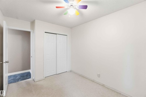 Wall-to-wall carpeting in a neutral tone, featuring a ceiling-mounted fan with multi-colored blades - 17303 107 Street, Edmonton, AB 