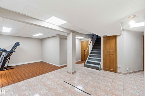 Lower level featuring a staircase with carpeted treads, varied tile flooring, recessed panel doors, and a drop ceiling with integrated lighting - 17303 107 Street, Edmonton, AB 