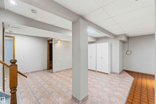 Finished lower level featuring light-toned tiled flooring, white walls, exposed support beams, built-in white cabinetry, and a textured drop ceiling - 17303 107 Street, Edmonton, AB 