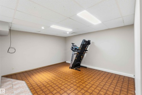 Spacious room featuring patterned brown floor tiles, light-toned walls, and a white drop ceiling with recessed lighting and two rectangular fluorescent fixtures - 17303 107 Street, Edmonton, AB 