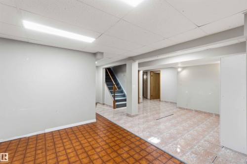 Finished lower level featuring a drop ceiling with fluorescent lighting, painted walls, and a combination of square tiled flooring and terracotta-toned flooring - 17303 107 Street, Edmonton, AB 