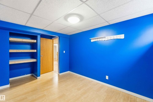 Room featuring wood-finish flooring, built-in shelving, a drop ceiling, and a flush-mount ceiling light fixture - 17303 107 Street, Edmonton, AB 