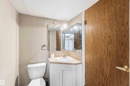 Compact bathroom featuring a white toilet, corner vanity with a round sink, and white cabinetry - 17303 107 Street, Edmonton, AB 