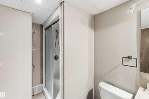 Compact bathroom with a glass-enclosed shower, white toilet, wall-mounted towel rack, and recessed ceiling lighting - 17303 107 Street, Edmonton, AB 