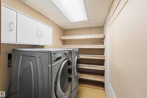 Utility room featuring built-in shelving, white wall-mounted cabinetry, and a drop ceiling with fluorescent lighting - 17303 107 Street, Edmonton, AB 