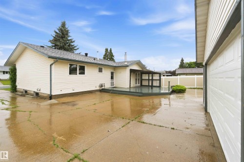 Rear exterior featuring vinyl siding, a multi-level deck with privacy screening, a concrete patio, and a detached garage with a paneled door - 17303 107 Street, Edmonton, AB 