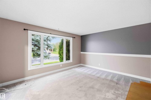 Spacious room featuring a large three-panel window with white framing, light-toned carpeting, and a two-tone wall design with a chair rail - 17303 107 Street, Edmonton, AB 
