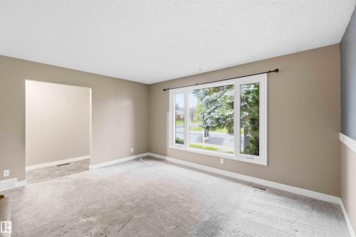 Bright living area featuring a large picture window, textured ceiling, light neutral wall paint, and white baseboards - 17303 107 Street, Edmonton, AB 