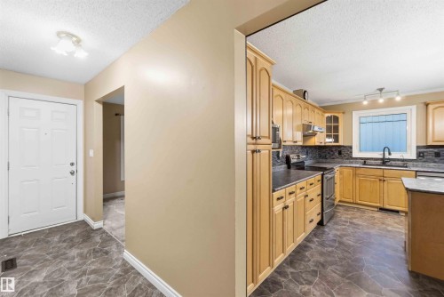 Kitchen featuring ample light wood cabinetry, dark countertops, stainless steel appliances, and a dark tile backsplash - 17303 107 Street, Edmonton, AB 